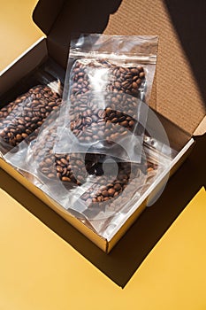 Roasted arabica sample coffee box with beans in blank transparent plastic bag with zipper on yellow background