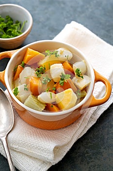 Roasted or baked root vegetables with fresh herbs, orange vegetables on plate. Vegan food