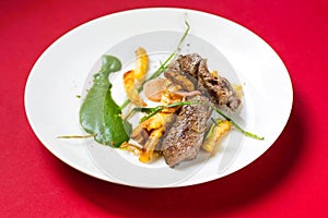 Roasted beef, french fries, spinach on white plate on red, closeup.