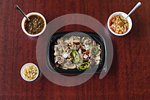 A roasted beef in a plastic container  accompanied  with Mexican salsas and white beans photo