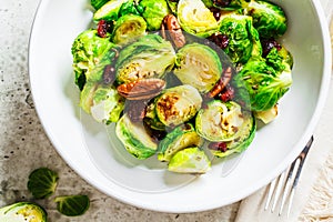 Roasted Brussels sprouts salad with cranberries and nuts in white bowl, top view. Healthy vegan food concept