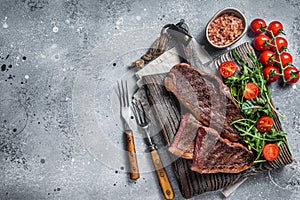 Roasted cap rump or Top sirloin beef meat steak on wooden board with salad. Gray background. Top view. Copy space
