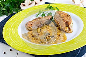 Roasted carp steaks with mushroom sauce on a plate on a white wooden background.