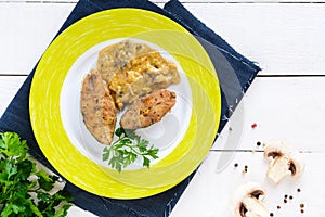 Roasted carp steaks with mushroom sauce on a plate on a white wooden background