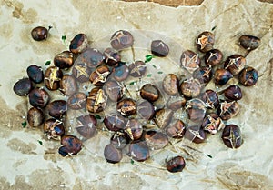 Roasted chestnuts on oily worn craft paper over rustic wooden background, top view.