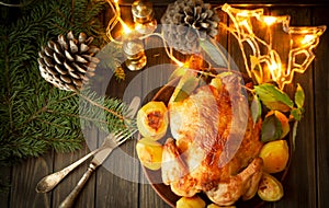 Roasted chicken on dark wooden background with holiday illumination