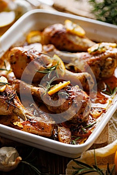 Roasted chicken legs drumsticks with rosemary, garlic and lemon in a ceramic baking dish