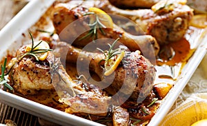 Roasted chicken legs drumsticks with rosemary, garlic and lemon in a ceramic baking dish