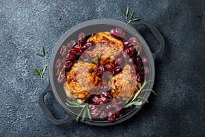 Roasted chicken legs with red grapes on pan over black slate stone background.