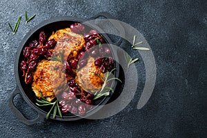 Roasted chicken legs with red grapes on pan over black slate stone background.