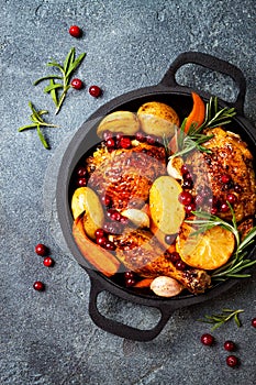 Roasted chicken legs with root vegetables, lemon, garlic, cranberry and rosemary on pan