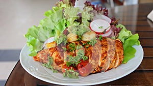 Roasted chicken with paprika, roasted tomatoes and garlic in white dish decorated with mixed vegetables as side dish