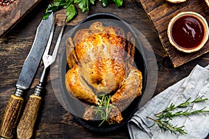 Roasted chicken with rosemary served on black plate with sauces on wooden table, top view.