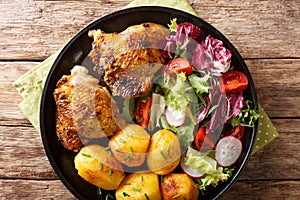 Roasted chicken thighs with new potatoes and fresh salad close-up on the plate. horizontal top view