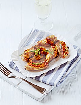 Roasted chicken wings with fresh rosemary on bright wooden background.