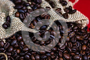 Roasted coffee beans in a burlap sack, sackcloth bag with coffee beans on red background, top view, coffee concept