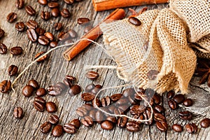 Roasted coffee beans , coarse burlap sac and cinnamon on old wooden table. Top view, grunge texture. With place for your