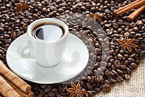 Roasted coffee beans with a cup on a saucer with an espresso drink with cinnamon and anise