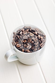 Roasted coffee beans in coffee cup on white table