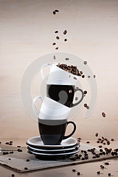 Roasted coffee beans falling down into black and white cups on the stack of the plates standing on newspaper.