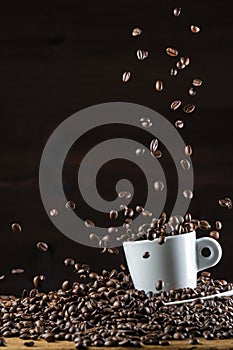 Roasted coffee beans falling down on white cup on wooden table