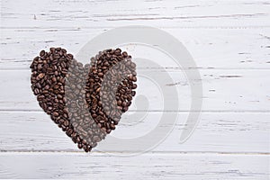 Roasted coffee beans in form of a heart on white wooden background.
