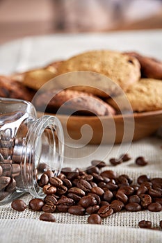 Roasted coffee beans get out of overturned glass jar on homespun tablecloth, selective focus, side view