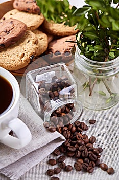 Roasted coffee beans get out of overturned glass jar on homespun tablecloth, selective focus, side view