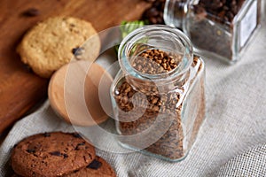 Roasted coffee beans get out of overturned glass jar on homespun tablecloth, selective focus, side view