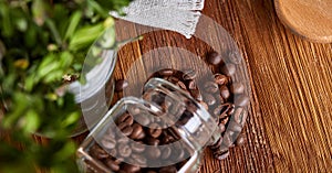 Roasted coffee beans get out of overturned glass jar on wooden background, selective focus, side view