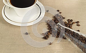 Roasted coffee beans in a glass bottle and a Cup of coffee on linen cloth