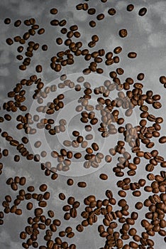 Roasted coffee beans lie across the entire frame on a surface with a patchy gray texture. View from above
