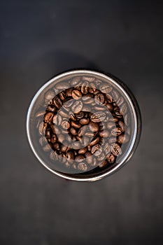 Roasted coffee beans in metal coffee grinder on black background top view