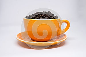 Roasted coffee beans in a orange ceramic mug with saucer on whit