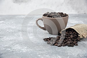 Roasted coffee beans out of burlap sack and in cup on marble background