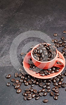 Roasted coffee beans in a red cup on black background.