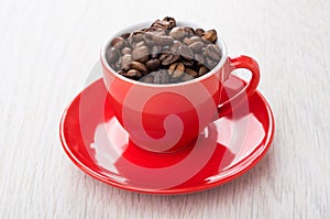 Roasted coffee beans in red cup on saucer on table