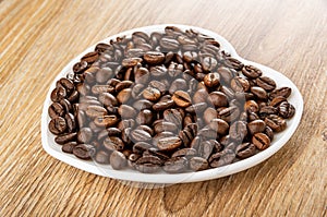 Roasted coffee beans in saucer in heart shape on wooden table