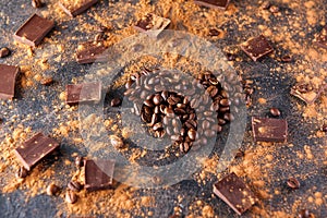 Roasted coffee beans in the shape of a heart on the dark stone background with dissipate cocoa, pieces of chocolate and beans. Sel