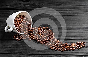 Roasted coffee beans spilling out of a white cup on the wooden table