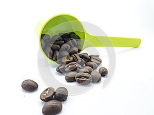 Roasted coffee beans spilling from a plastic spoon over a white background