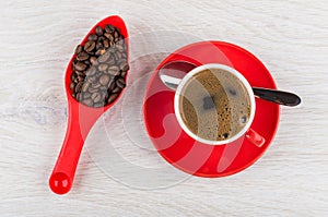 Roasted coffee beans in spoon, coffee in cup on saucer