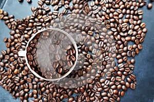 Roasted coffee beans texture with coffee beans scattered on dark background and white cup â€“ top view