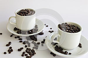 Roasted coffee beans in two coffee cups , on white isolated background