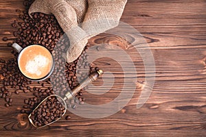 Roasted coffee beans waking up from a jute coffee bag on an wooden table. Close-up. Cup of coffee.