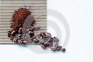 ROASTED COFFEE BEANS IN A WHITE CERAMIC BOWL WITH GROUNDS ON CORRUGATED CARDBOARD AND WHITE CANVAS BACKGROUND