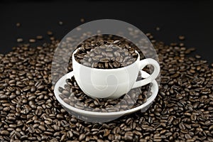 Roasted coffee beans in a white coffee cup on coffee beans field background