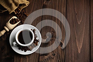 Roasted coffee beans with a white cup of espresso on a dark wooden table, rustic, top view