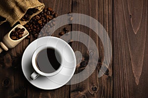 Roasted coffee beans with a white cup of espresso on a dark wooden table, rustic, top view