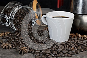 Roasted coffee beans with a white cup and moka pot.Espresso italian coffee maker on dark rustic wooden background with copy space